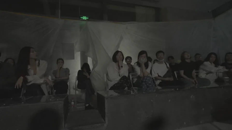Spectators remain visible behind translucent fabric beneath the exit light.