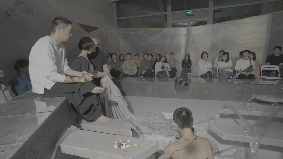 The live site holds performers, spectators, stage surfaces, and the camera in one field.